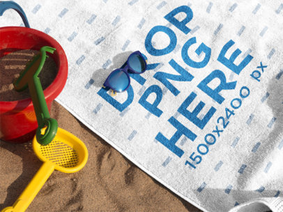 Mockup of a Towel Lying on the Beach with Accessories Near it and Sunglasses