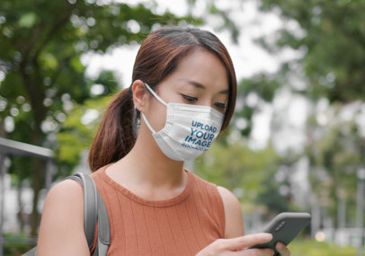 Face Mask Mockup of a Woman Checking Her Mobile Phone at a Park
