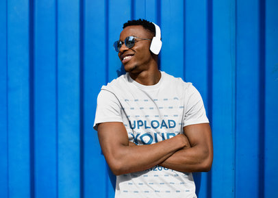 Tee Mockup of a Man with Headphones Leaning over a Colorful Wall