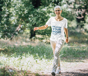 T-Shirt Mockup of a Happy Senior Woman Walking in the Forest 