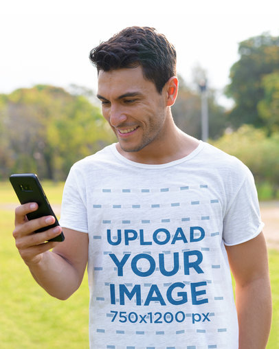 T-Shirt Mockup of a Happy Man Checking His Phone at a Park 