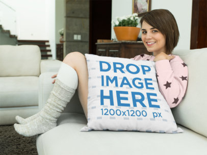 Young Woman Holding a Square Pillow Mockup While Sitting in her Sofa