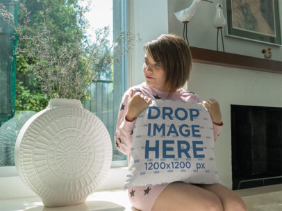Young Woman Looking at a Plant While Holding a Square Pillow Mockup Sitting Down