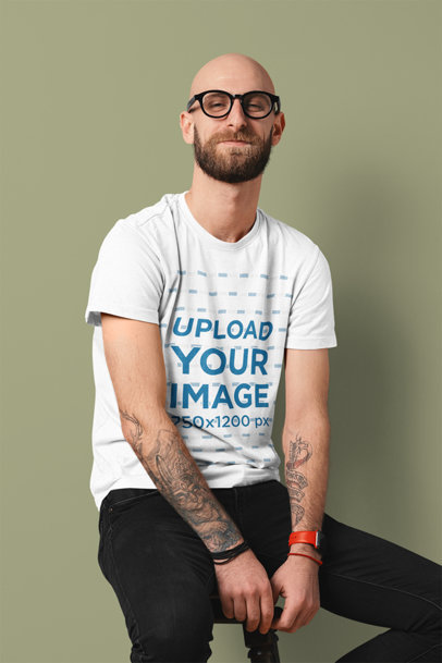 Basic T-Shirt Mockup of a Tattooed Man Sitting Against a Colored Backdrop 