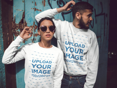 Hispanic Couple Wearing Different Crewneck Sweatshirts Mockup While Standing Against an Old Door