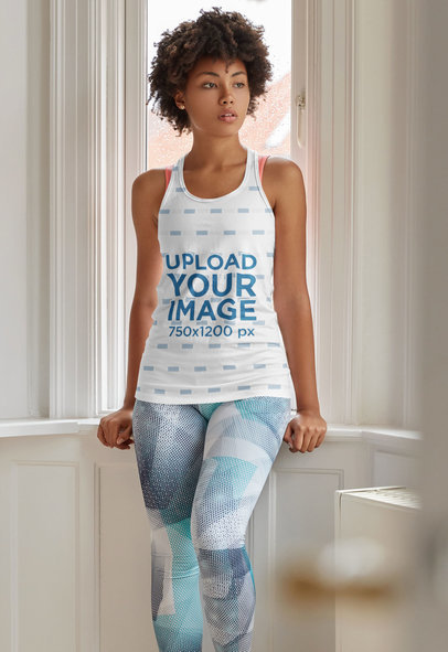 Mockup of a Woman Wearing a Sublimated Tank Top and Posing by a Window
