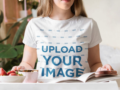 T-Shirt Mockup of a Young Woman Reading While Having Breakfast