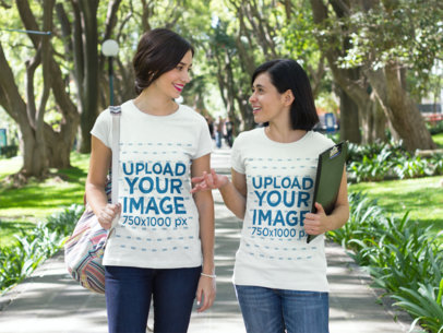 Two Hispanic Girls Wearing Different Tees Mockup While Walking and Talking at the Park a15658