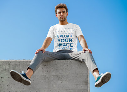 T-Shirt Mockup of a Young Man Sitting On Top of a Concrete Wall