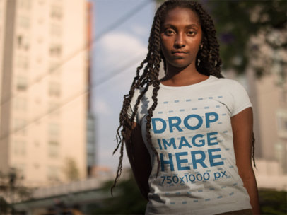 Mockup of a Woman Wearing a T-shirt While Standing Against Blurry Buildings in the City 
