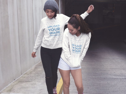 Two Girlfriends Wearing a Crewneck Sweatshirt and a Pullover Hoodie Mockup with Different Designs While Playing in the City