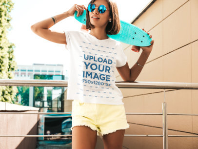 T-Shirt Mockup of a Young Woman Holding a Penny Board Over Her Shoulder