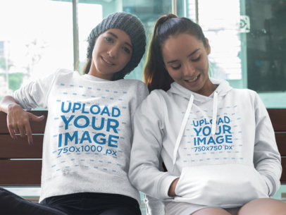 Two Young Women Sitting Down Together Wearing a Crewneck Sweatshirt and a Pullover Hoodie Mockup with Different Designs