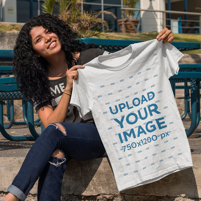 Young Happy Customer Showing a T-Shirt Template While Sitting Down Outdoors