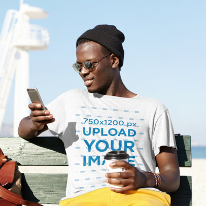 T-Shirt Mockup of a Man Checking His Phone by the Beach