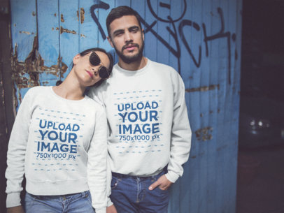 Happy Couple Wearing Different Crewneck Sweatshirts Mockup While Standing Against a Blue Door