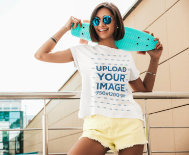 T-Shirt Mockup of a Joyful Young Woman Holding a Small Skateboard 