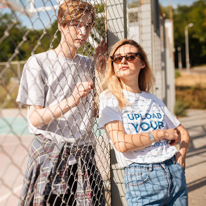 T-Shirt Mockup Featuring a Young Woman With Sunglasses Posing Against a Fence 