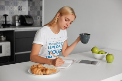 T-Shirt Mockup Featuring a Woman Writing While Having Breakfast 