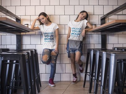 Pair of Women Wearing Round Neck Tees Mockup while Standing Bored Against a White Tiles Wall