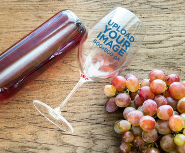 Mockup of a Wine Glass Lying over a Wooden Surface Next to a Bunch of Grapes