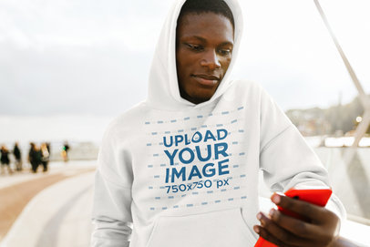 Mockup of a Man in a Hoodie Checking His Phone