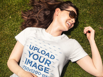 Smiling Woman Lying Down on the Grass While Wearing a Round Neck T-Shirt Template and Sunglasses
