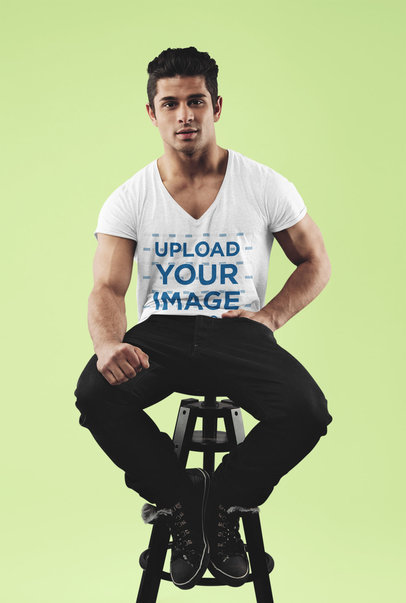T-Shirt Mockup Featuring a Young Man Sitting on a Stool at a Studio 