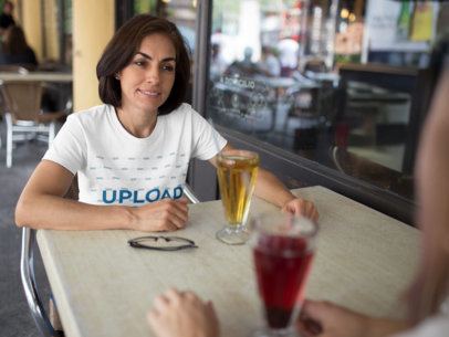 Mockup of a T-Shirt Being Worn by a Woman While Talking to a Friend in a Cafe