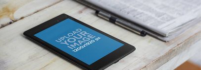 Mockup of a Black Nexus 7 in Portrait Mode Next to a Newspaper