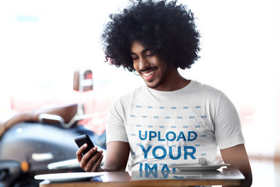 T-Shirt Mockup of a Happy Man With Curly Hair Checking His Phone at a Restaurant 