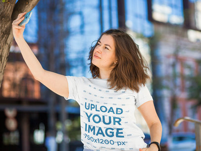 T-Shirt Mockup of a Woman Taking a Selfie on the Street
