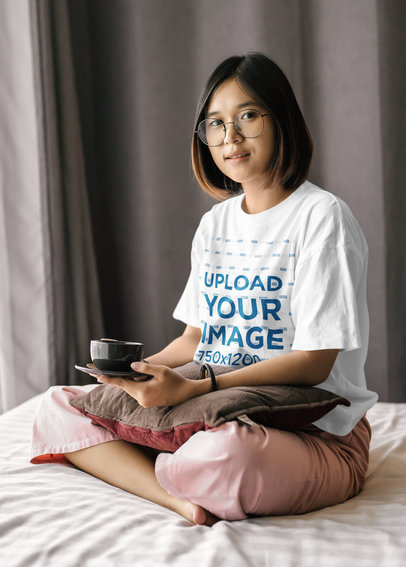 Oversize T-Shirt Mockup of a Woman with Glasses Having Tea on Her Bed