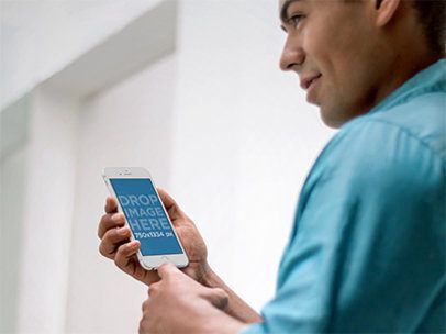 Mockup of a Young Man in a Blue Shirt Using an iPhone 6