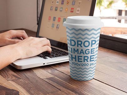 Coffee Cup Mockup Featuring a Woman Using a Macbook Pro at a Café
