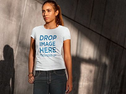 T-Shirt Mockup of a Woman Standing Next to a Concrete Wall