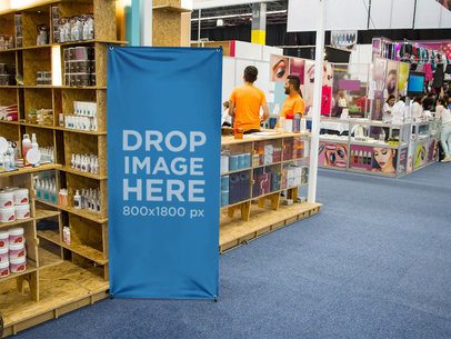 Vertical Banner Mockup Standing Next to a Beauty Stand at a Trade Show