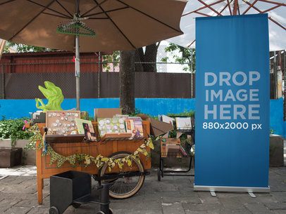 Roll Up Banner Mockup Next to a Merchandise Cart Outdoors a11273