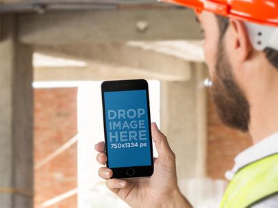 Mockup of a Man Checking His iPhone in Portrait Mode in a Construction Zone