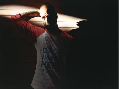 Man Wearing a Raglan T-Shirt with his Arm Back in a Dark Room