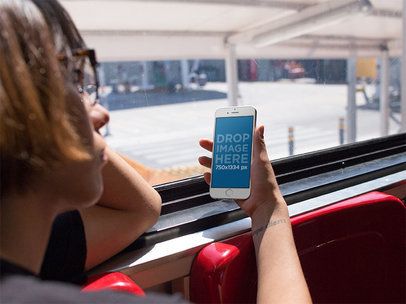 Mockup of a Woman Holding an iPhone in Portrait Position During a Bus Ride