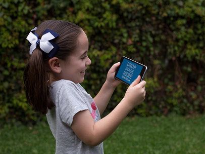 Little Girl Playing on her Black iPhone 7 Plus in Landscape Position Mockup in the Back Yard