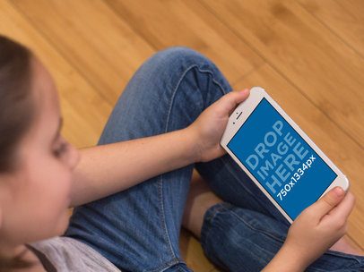 Mockup of a Girl Sitting on a Wooden Floor Holding an iPhone in Landscape Position 
