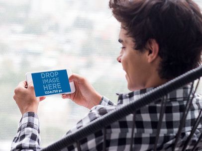 Mockup of a Young Man Staring at an iPhone in Landscape Position with Blurry Background