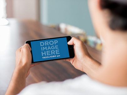 Young Man Playing with his iPhone 6 Plus in Landscape Position Mockup at Home a13042