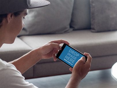 Mockup of a Teen Playing on his iPhone 7 Plus in Landscape Position in his Living Room