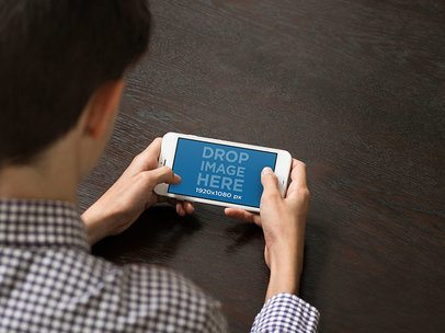 Young Boy Playing with his iPhone 7 Plus in Landscape Position Mockup at a Table 