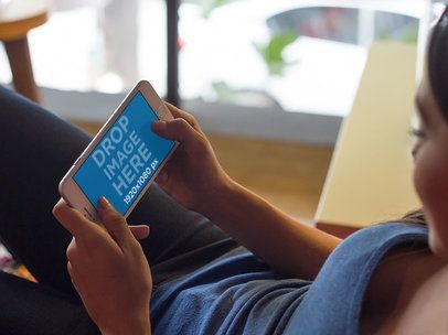 Mockup Featuring a Woman Lying on a Couch Staring at an iPhone