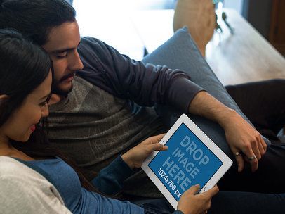 White iPad Mockup in Landscape Position of a Couple Lying on a Couch in their Apartment