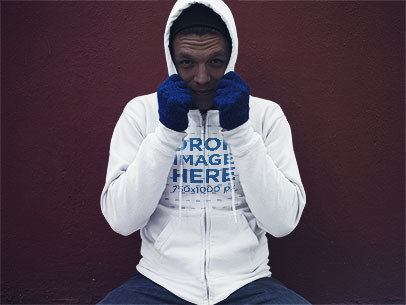 Young Man Wearing a Pullover Hoodie Sitting in Front of a Red Wall Mockup a13198